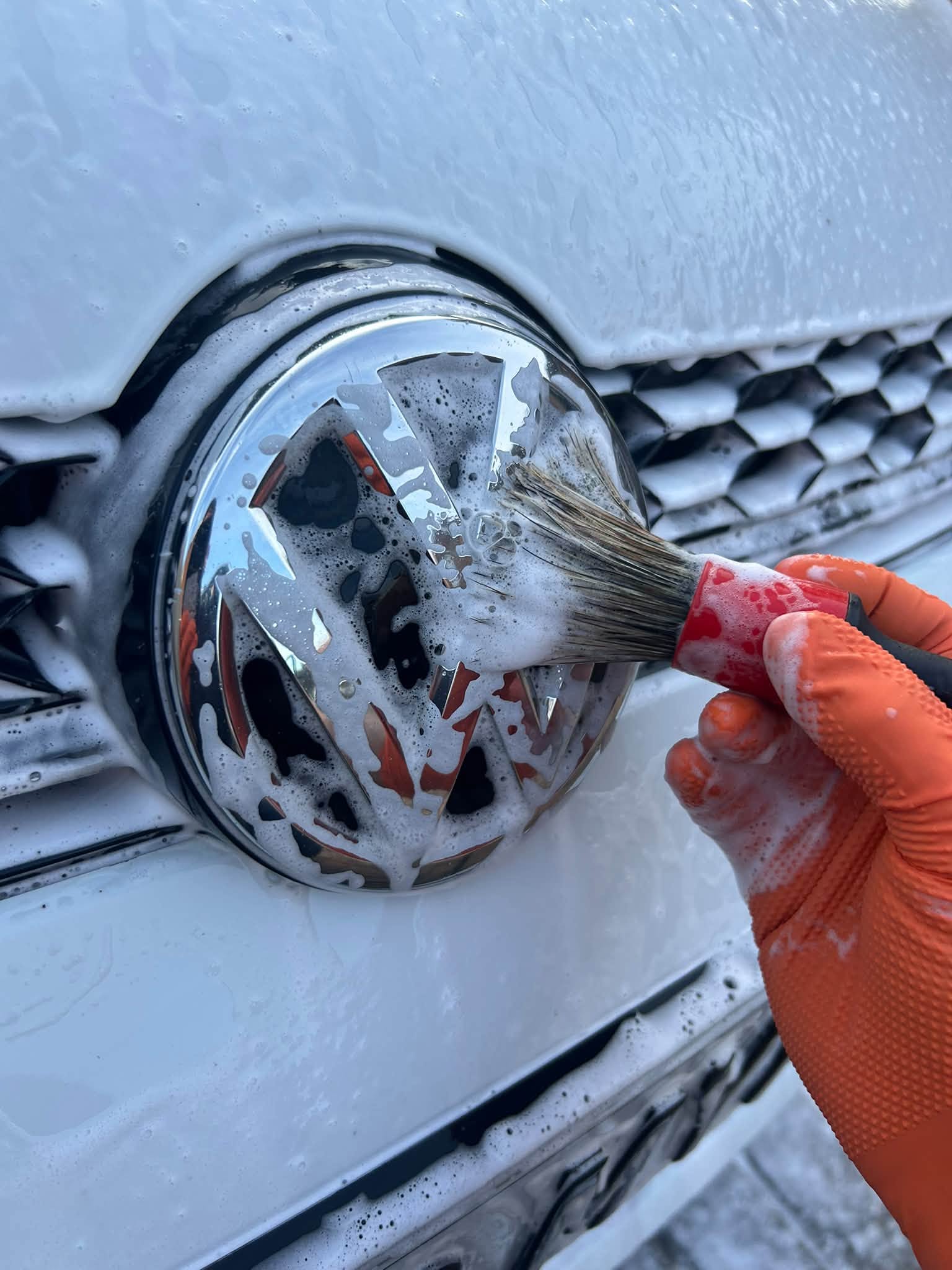 Gloved hand brushing snow foam around a Volkswagen badge on a white Golf