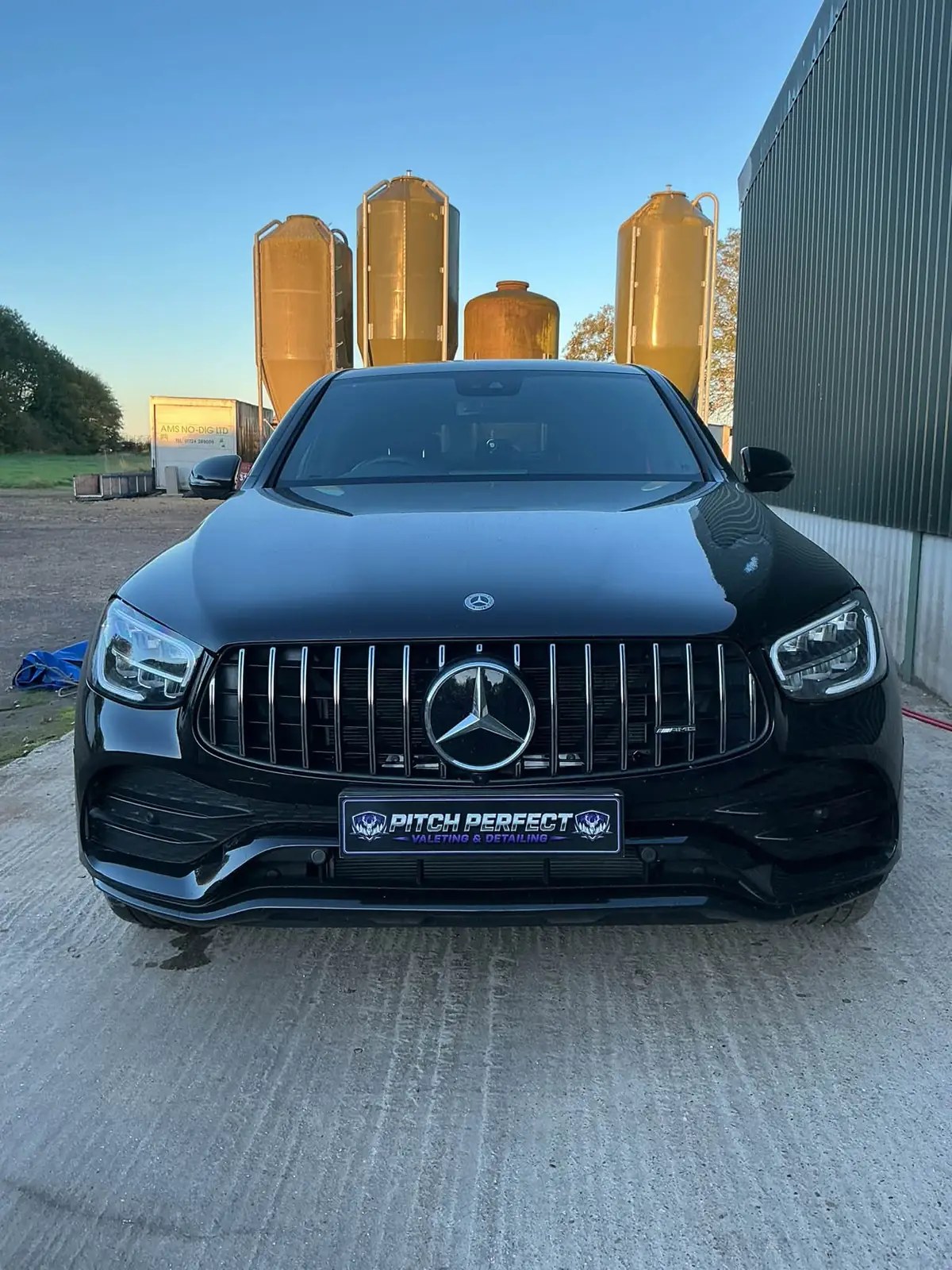 Black Mercedes GLC with a Pitch Perfect plate parked in front of grain silos