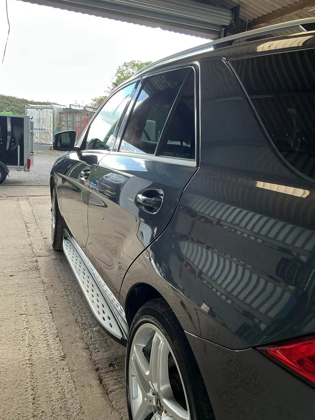 Dark grey Mercedes SUV with side steps and glossy paint under a barn roof