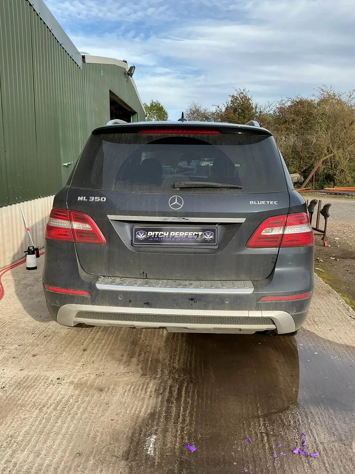 Dusty rear of a Mercedes ML350 on wet concrete beside a green shed