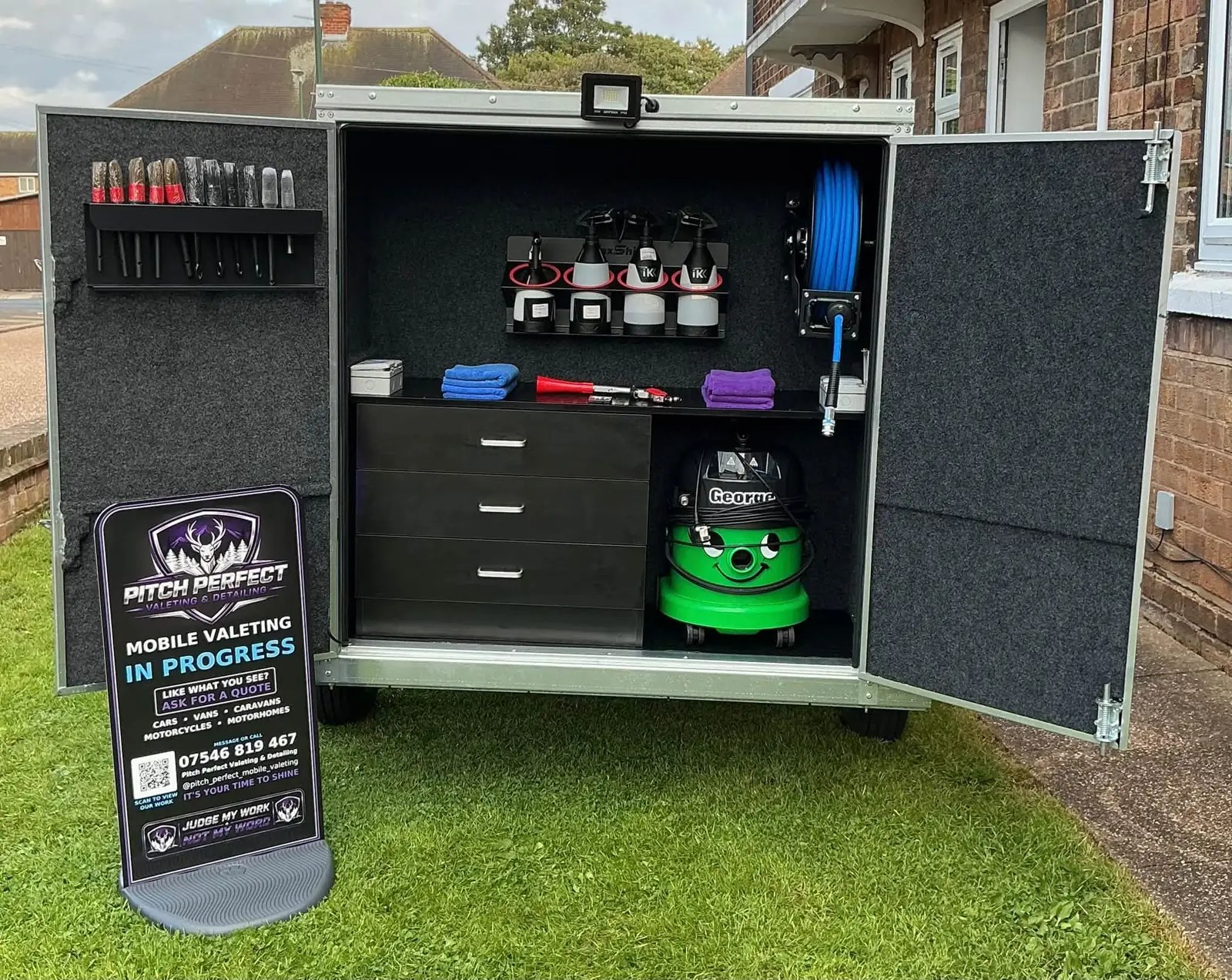 Open valeting trailer with shelving, tools, a green vacuum and Pitch Perfect sign