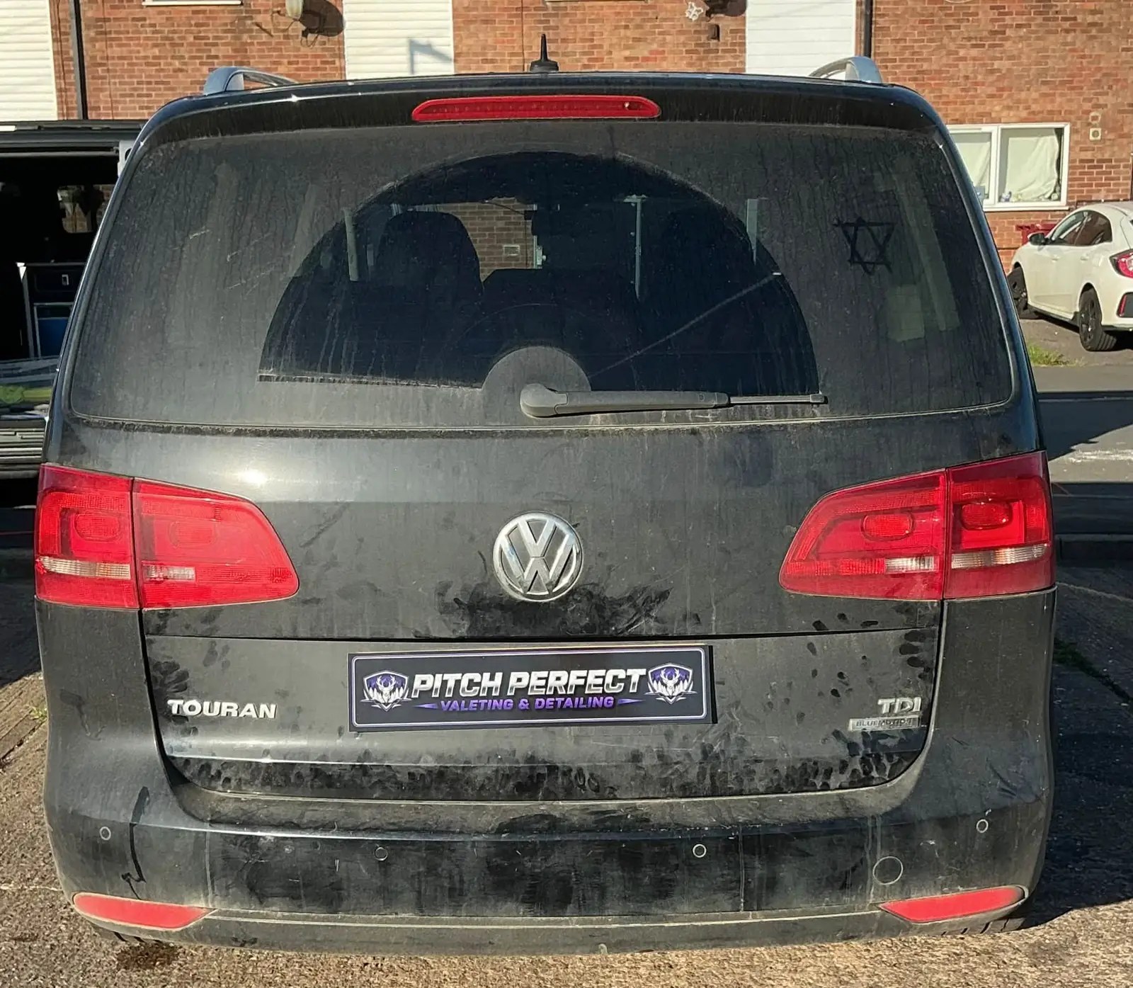 Rear of a black Volkswagen Touran covered in dusty road film