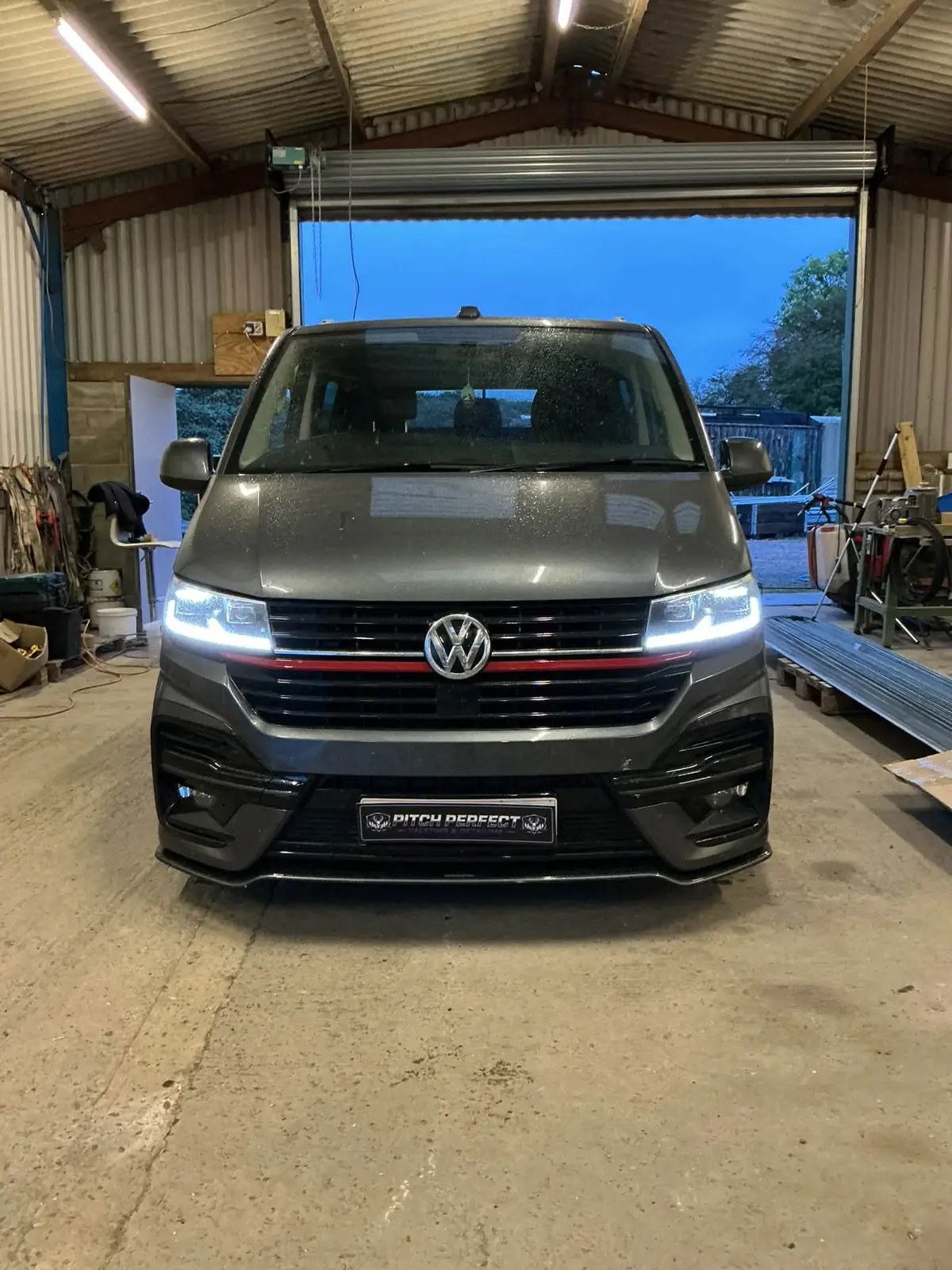 Dark grey Volkswagen Transporter with red grille stripe parked inside a barn